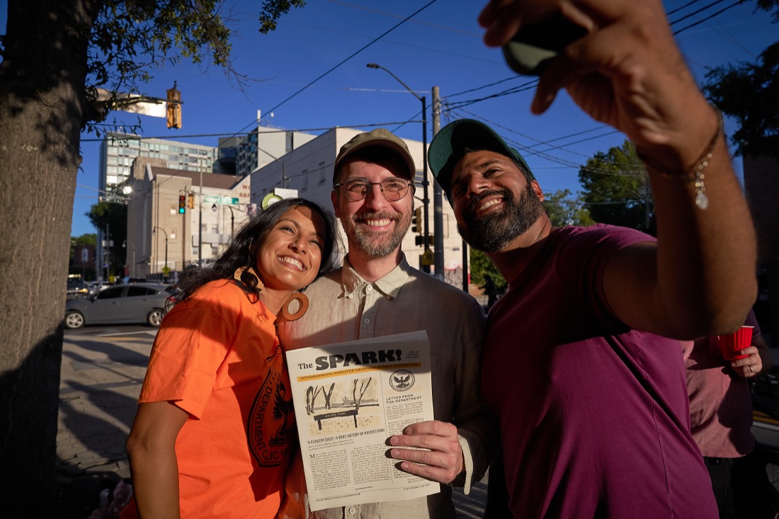 Three people smiling and holding a copy of The Spark on an Atlanta sidewalk